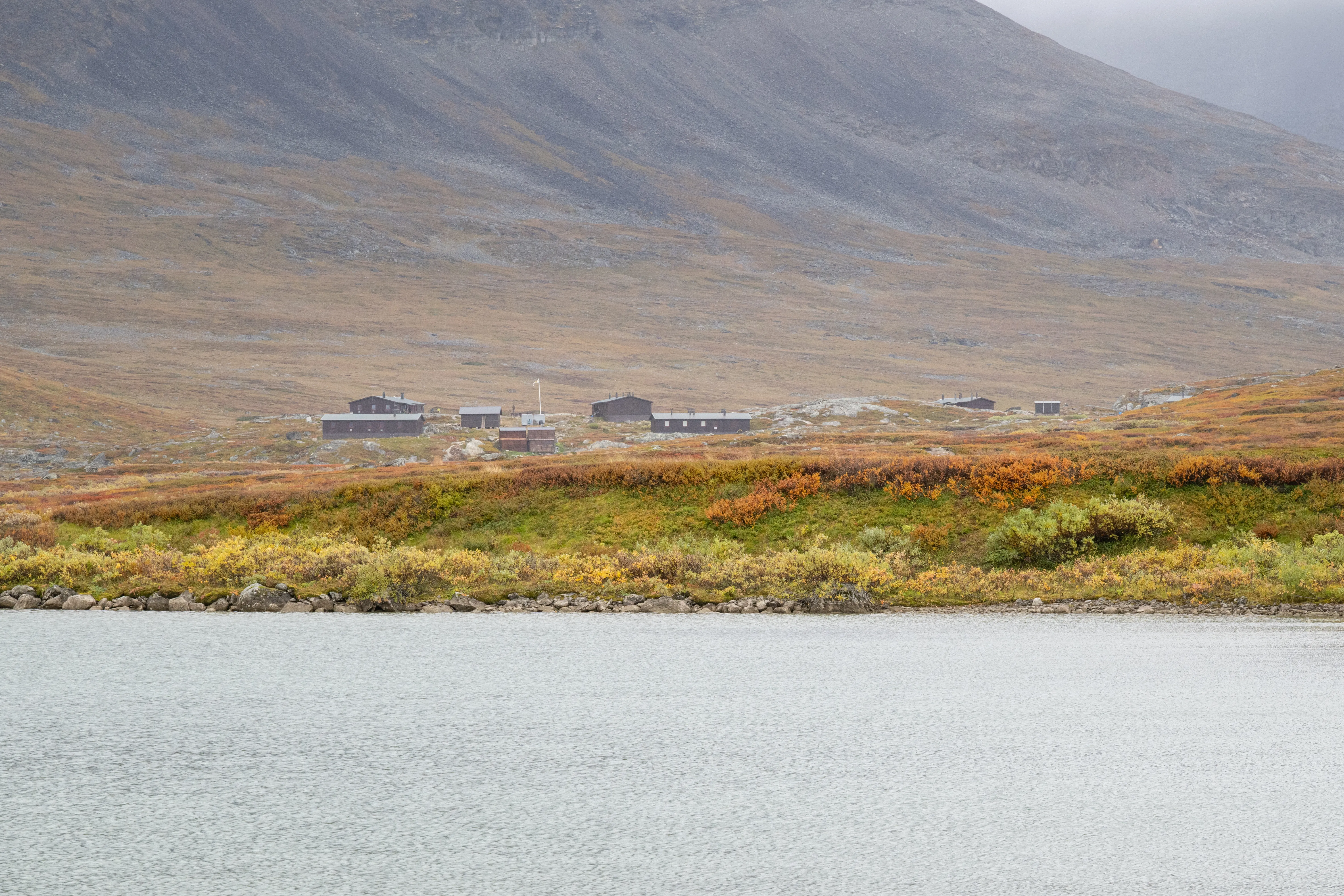 Un paysage sauvage de Laponie aux couleurs automnales, où quelques refuges se nichent au pied des montagnes, au bord d’un lac paisible.